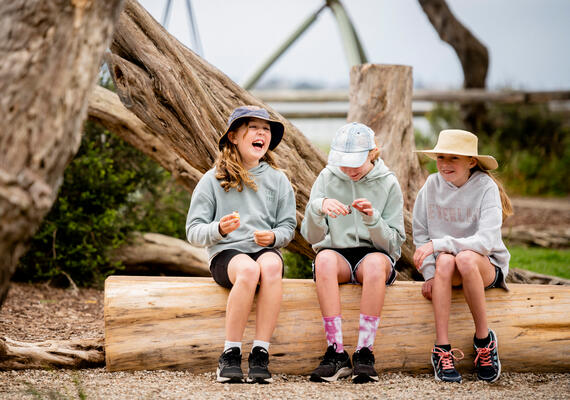 three chidren sit on a log laughing 