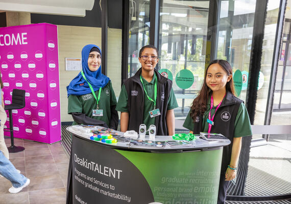 Three DeakinTALENT student volunteers at a promotional stall.