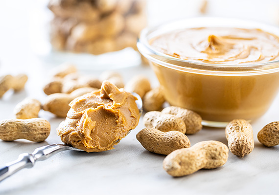 Small bowl and spoonful of peanut butter with peanuts scattered around