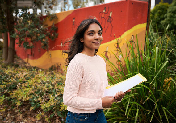 Deakin business student walks past an Indigenous art wall on campus.