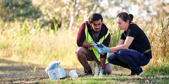 Two students examine water samples outdoors.