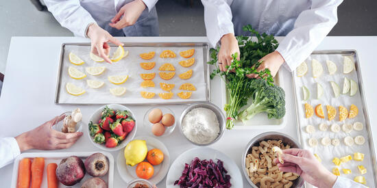 A restaurant scene with two people laying down slices of lemon on a tray and pulling parsley off the stem