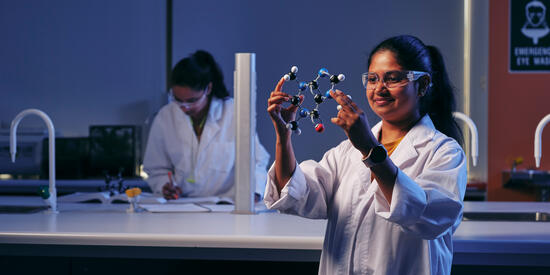 Deakin student in a science lab holds a molecule model wearing safety glasses.