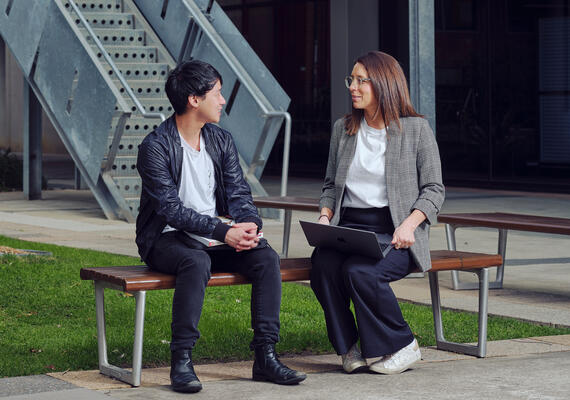 A male and female adult siting on a park bench side-by-side