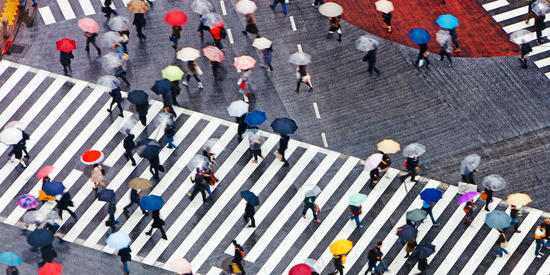 Aerial shot of people walking on pedestrian crossing with colourful umbrellas.