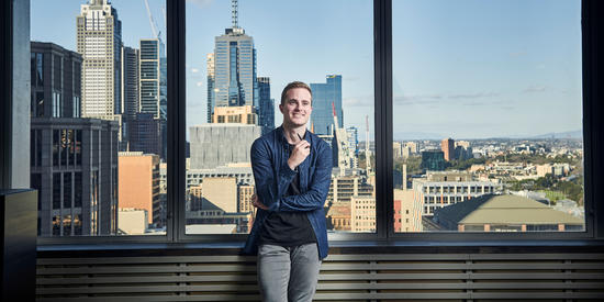 Student from a Deakin property and real estate course stands in front of a window with the city skyline behind him.