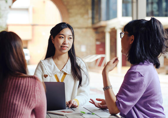 Three deakin students on campus around a table seated