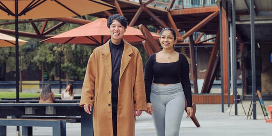 Two Deakin students walking in an outdoor courtyard on campus.