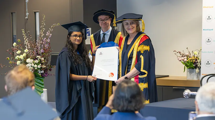 Deakin Chancellor Claire Higgins and Caretaker Vice-Chancellor Deakin Distinguished Professor Matthew Clarke present a graduate with their testamur at a Sensory Friendly Ceremony. 