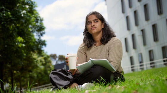 A Deakin master of arts students sits on grass. 