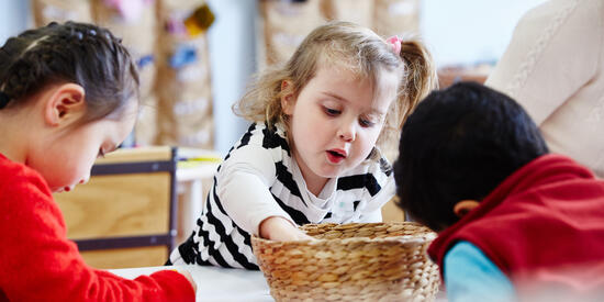 Young child reaching into straw basket at childcare