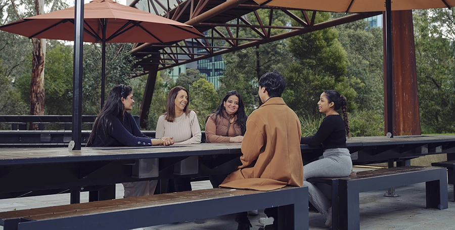 Four Deakin students sit under an umbrella in the Melbourne Burwood Campus cafe.