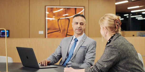 Two corporate workers talking with a laptop in hand at a desk