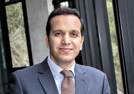 A close up of a person, Fethi Mansouri, smiling at the camera and wearing a suit. 