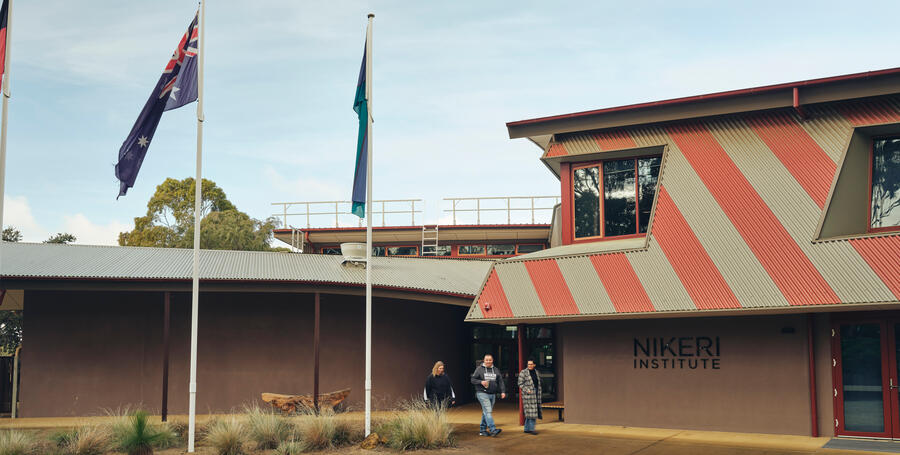 A wide view of students walking outside the NIKERI Institute, Deakin University. Flags are flown. 