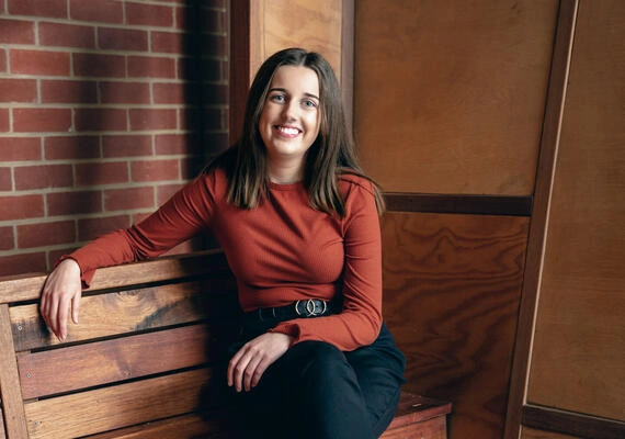 Student smiling into camera in front of brick wall