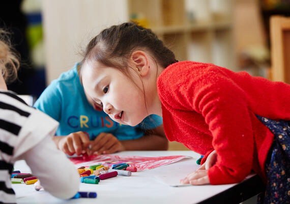 Young child in red shirt looking at art on piece of paper in childcare.