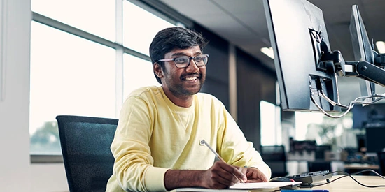 A Deakin postgraduate student looking at a computer screen and taking notes.