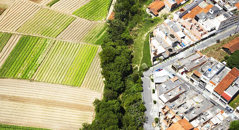 Aerial view of fields on the left, a thin strip of trees in the middle and urban sprawl of houses to the right.