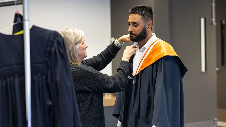 A graduate at a Sensory Friendly Ceremony puts on their academic robes. 