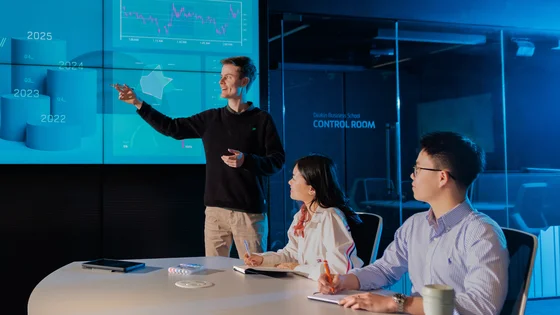 A student making a presentation in front of a large screen showing business data.
