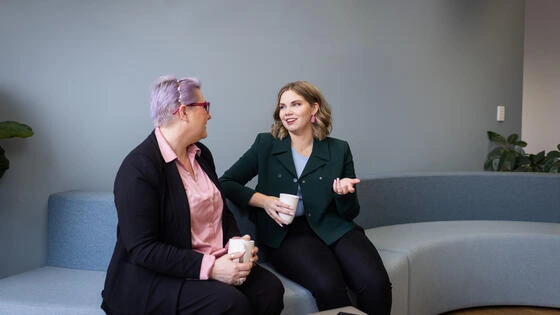 A Deakin master of business student sits on a couch talking to another student