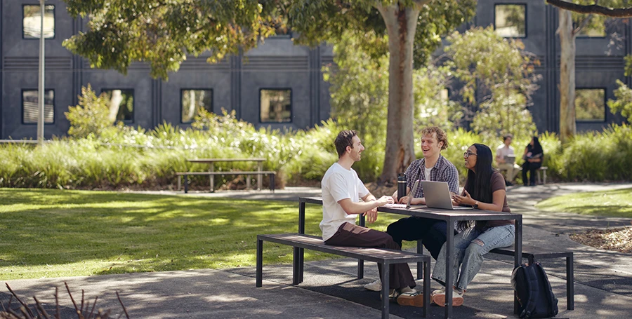 Deakin students sit around a table on the Melbourne Burwood Campus lawn.