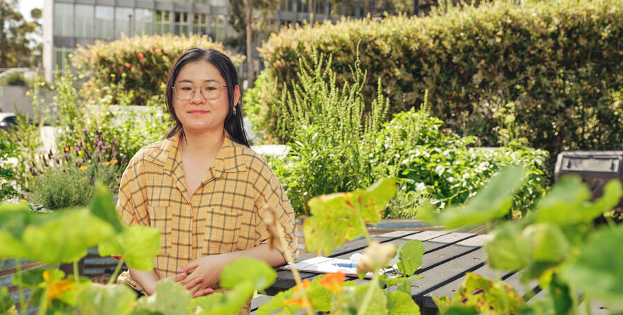 A woman sits in a green garden at the Deakin Burwood Campus.