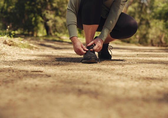 A close up picture of a runner tying their shoes on a running trail