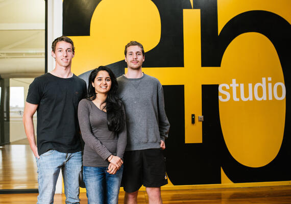 Three students in front of an A+B Studio banner on the wall