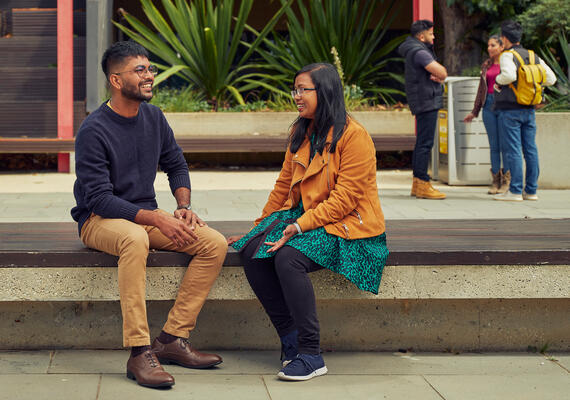 Two deakin students sitting and talking on campus.