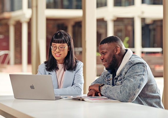 Two Deakin students sit at a table looking at a laptop at the Deakin Geelong Waterfront Campus.