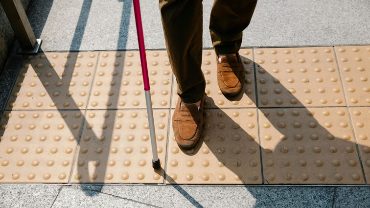 Image of a person's feet walking on a footpath with a white cane 