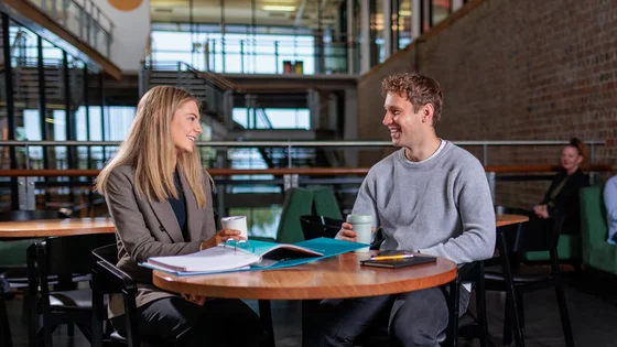 Two students in conversation sitting at a table.