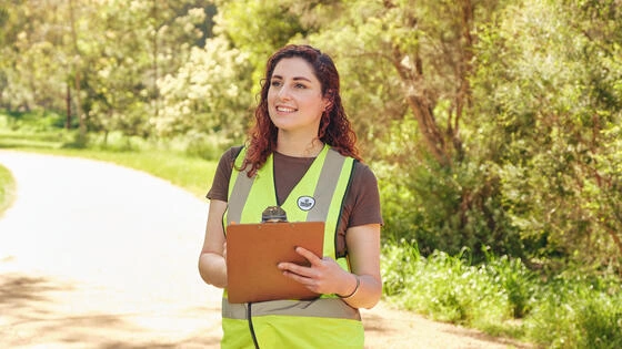 Deakin graduate diiploma of sustainability student stand in nature with high-vis vest and clipboard.