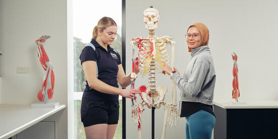 Two Deakin students examine a model skeleton to learn about biomechanics.