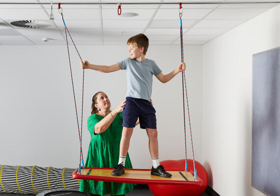 Child standing on an occupational therapy swing with a Deakin occupational therapist.