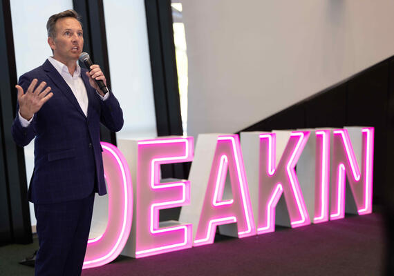 Corporate worker giving a speech in front of a Deakin neon sign