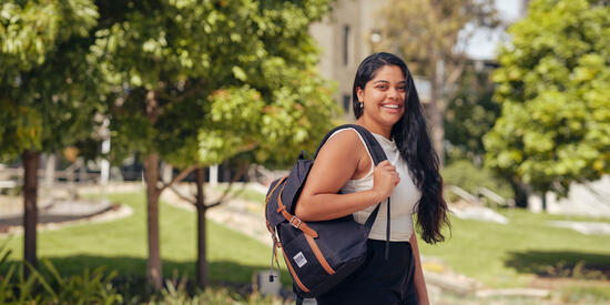 A smiling student wearing a backpack and standing outside.