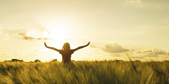 Person standing outside in tall grass enjoying the sunshine.