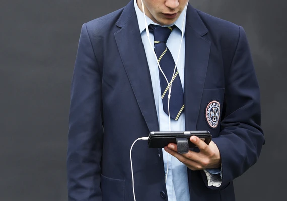 A young person in a school uniform looking at a phone.