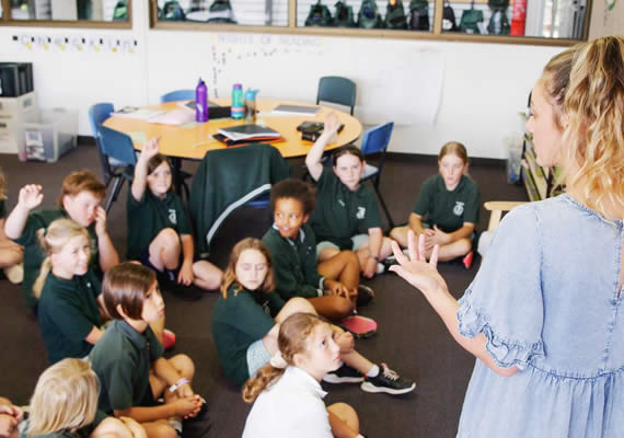 Teacher talking with seated class of primary school students.