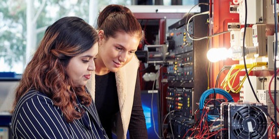 Two colleagues stand next to each other examining electrical wires.
