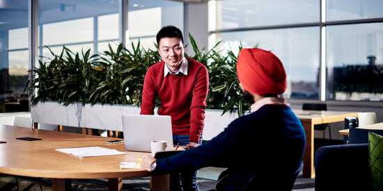 Two Deakin work and wellbeing students having a conversation. They are standing around a laptop in a meeting room.