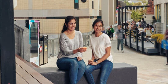 Two Deakin students sit on a wall at Deakin Melbourne Burwood Campus.