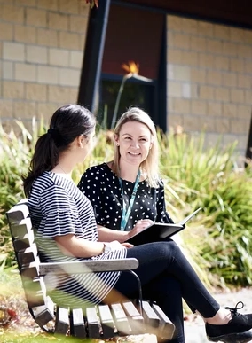 Two students talking while seated on an outdoor bench.