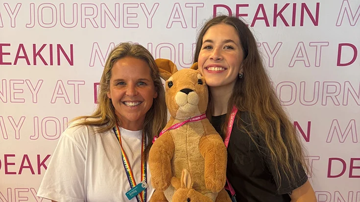 Zoe and a peer in front of a Deakin banner, holding a toy kangaroo and joey