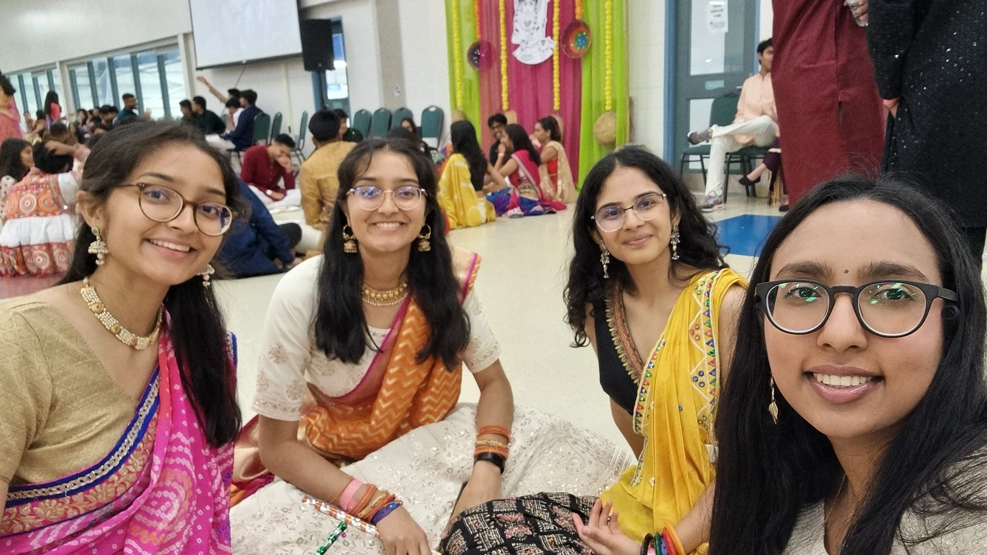 Kaviya and three friends sitting, smiling at the camera. They are wearing traditional Indian dress.
