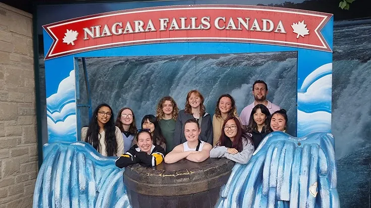 Kaviya and 11 other people pose in a large frame with a red and white sign at the top that reads "Niagara files Canada"