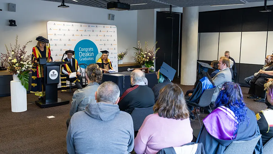 Graduands and their families seated at a Sensory Friendly Ceremony. Chancellor Claire Higgins is speaking at the front of the room.